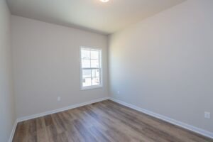 Empty room with light gray walls, wood laminate floor, and a window letting in natural light.