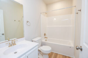A clean bathroom with a white sink, toilet, and bathtub. It has a wooden floor and beige walls.