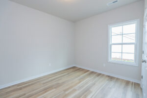 Empty room with light wood flooring, white walls, and a large window.