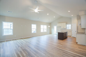Spacious, unfurnished open-plan room with wooden floors, kitchen island, ceiling fan, and large windows.