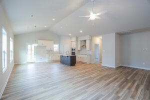 Spacious empty kitchen and living area with wood flooring, ceiling fan, and recessed lighting.