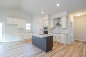 Modern kitchen with island, white cabinets, stainless steel appliances, and wooden floor. Bright lighting.