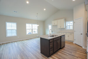 Modern kitchen with island, wood floors, white cabinets, large windows, and high ceiling.