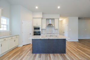 Modern kitchen with island, wooden floors, white cabinets, stainless steel appliances, and subway tile backsplash.