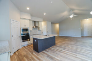 Modern kitchen with a central island, white cabinets, stainless steel appliances, and wooden flooring.
