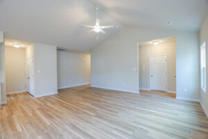 Spacious empty room with wooden floors, light walls, ceiling fan, and closed white doors.