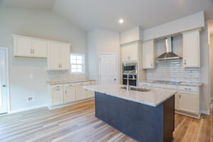 Modern kitchen with marble countertops, white cabinets, a central island with sink, and stainless steel appliances.