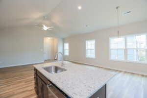 Open living area with island kitchen, hardwood floors, ceiling fan, and large windows for natural light.