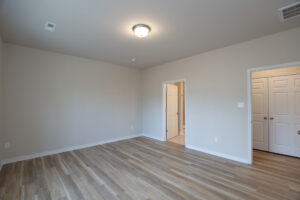 Vacant room with light wood flooring, a ceiling light, a door to a bathroom, and closet with double doors.