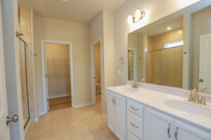 Bathroom with double sinks, large mirror, walk-in shower, and a separate area leading to a closet and toilet.