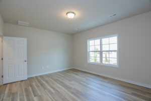 Empty room with wood floor, white walls, ceiling light, window, and open door.