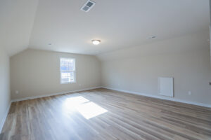 Empty room with light wood flooring, a window letting in daylight, and a ceiling light fixture.