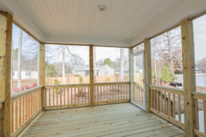 Wooden deck with railing, screened enclosure, and a view of a backyard with trees and neighboring houses.