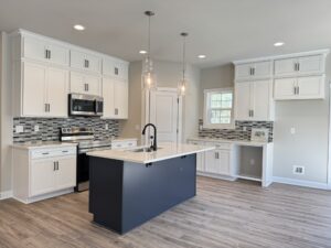 Modern kitchen in new homes in Richmond VA with white cabinets, black island, and a gray tile backsplash.