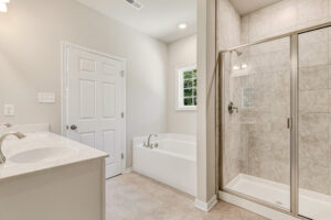 Modern bathroom in Lot 57, Patrick Henry Heights with double sinks, bathtub, glass shower, and tiled floor.