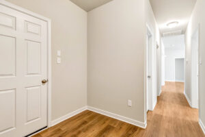 A bright hallway in Patrick Henry Heights, Lot 57, with wooden floors, white walls, and doors under ceiling lights.