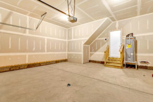 Unfinished garage at Lot 57, Patrick Henry Heights with drywall, concrete floor, water heater, and small wooden stairs.