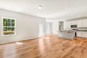 Bright, modern open-plan kitchen at Lot 57, Patrick Henry Heights with wood floors, white cabinets, and large windows.