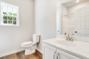 Bright bathroom in Lot 57, Patrick Henry Heights; white vanity and toilet, wood floor, and window with green views.
