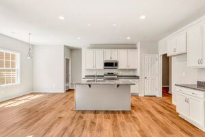 Bright kitchen in Patrick Henry Heights with white cabinets, granite island, stainless appliances, and light wood floors.