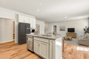 Bright modern kitchen with island in Lot 57, open to living room with sofa, TV, and wooden floors.