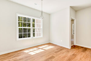 Bright, empty room in Patrick Henry Heights with large window, wood floor, and a hanging light fixture. Lot 57.