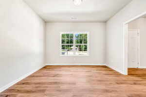 Bright, empty room in Patrick Henry Heights with wood floors, greenery views, and a door to the right. Lot 57.