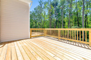 A wooden deck with railing on Lot 57 overlooks a green forest in Patrick Henry Heights on a sunny day.