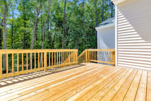 A sunlit wooden deck at Patrick Henry Heights Lot 57, attached to a house and overlooking a lush green forest.