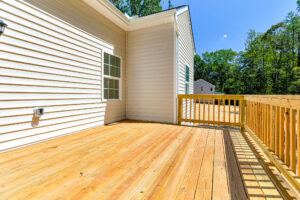 A sunlit wooden deck on Lot 57, attached to a light-colored house in Patrick Henry Heights, with trees behind.