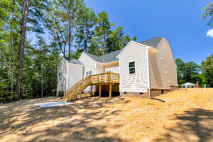 Charming white house with deck and stairs on Lot 57 in Patrick Henry Heights, surrounded by woods and blue skies.