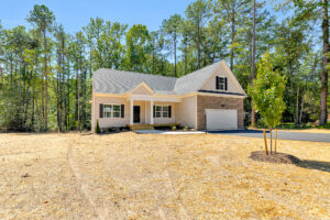 Single-story home on Lot 57 in Patrick Henry Heights, with front porch, garage, and newly seeded lawn among tall trees.