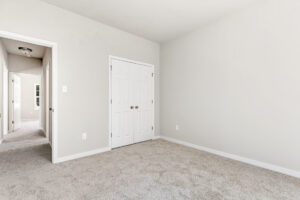 Empty room with beige carpet, white closet doors, and hallway in Patrick Henry Heights Lot 57.