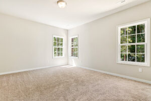 Empty room in Patrick Henry Heights, Lot 57, with beige carpet, white walls, and large windows letting in natural light.