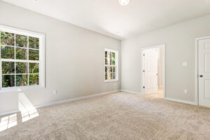 Bright, empty carpeted room in Patrick Henry Heights with two windows, white walls, and a door to an adjoining bathroom.