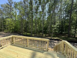Wooden deck with railings at Lot 57 in Patrick Henry Heights, overlooking a sunny forest and clear blue sky.