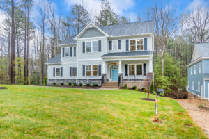 Two-story white house with a blue door in Patrick Henry Heights, set in a grassy yard surrounded by trees.