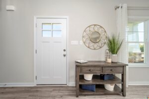 Modern entryway in Poplar Village with a white door, decorative mirror, table with plants, and woven baskets on wood flooring.