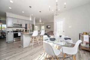 Modern kitchen in Poplar Village with white chairs, glass dining table, island, stainless steel appliances, and wooden flooring.