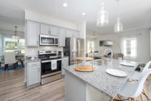 Modern kitchen in Poplar Village with gray cabinets, stainless steel appliances, island, pendant lights, and dining area.