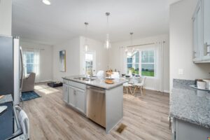 Modern kitchen and dining area in Poplar Village with light wood floors, gray cabinets, and large windows welcoming natural light.