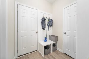 A small hallway in Poplar Village with white doors, a coat rack, kids backpack, blue umbrella, and bins beneath a bench.