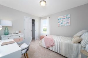 Bright bedroom in Poplar Village with a single bed, desk, chair, and soft pastel decor. Open closet and window with natural light.