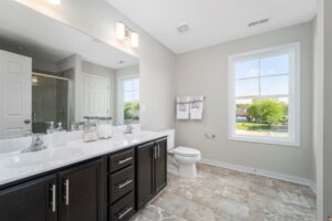 Located in Poplar Village, this modern bathroom features double sinks, a large mirror, toilet, and shower with ample natural light.