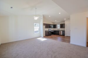 Empty living area with beige carpet and ceiling fan, beside a modern kitchen—ideal for new homes in Richmond VA.