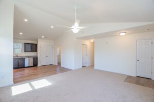 Open living area with beige carpet, ceiling fan, and kitchen view—perfect for new homes in Richmond VA.
