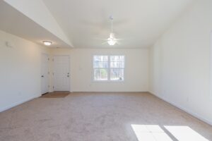 Sunlit living room with beige carpet, white walls, and ceiling fan in one of the new homes in Richmond VA.