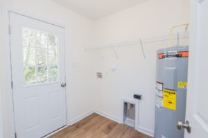 Laundry room in new homes in Richmond VA features a door, wire shelf, water heater, and outlets for washer and dryer.
