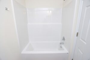 White bathtub with shower in a minimal bathroom—perfect for new homes in Richmond VA, featuring clean white walls and door.