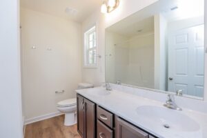 Bright bathroom in new homes in Virginia features double sinks, large mirror, and wood-style flooring.